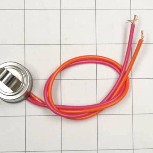 A metal can-style thermostat component with a dark body and two spade terminals, resting on a white grid.